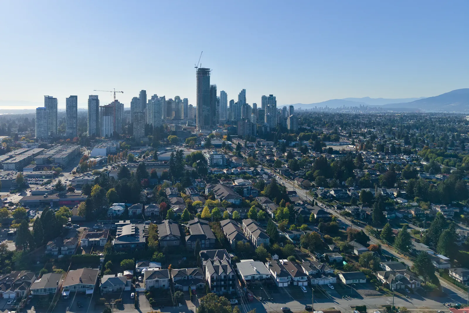 Metrotown skyline on a clear afternoon, with cranes on the towers and low-rise commercial buildings and homes in the foreground